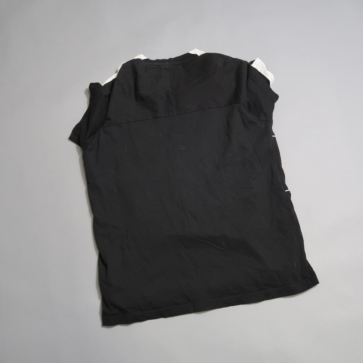 Black, sleeveless shirt laid flat on a light gray surface.