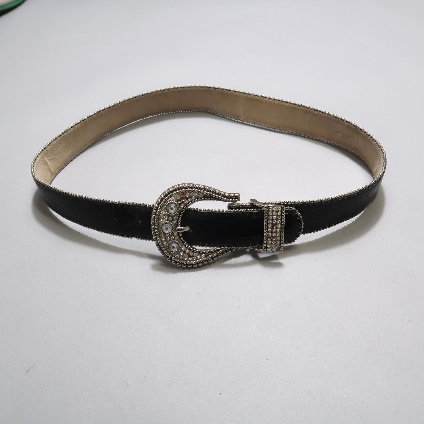 Black leather belt with an ornate silver buckle on a plain backdrop.