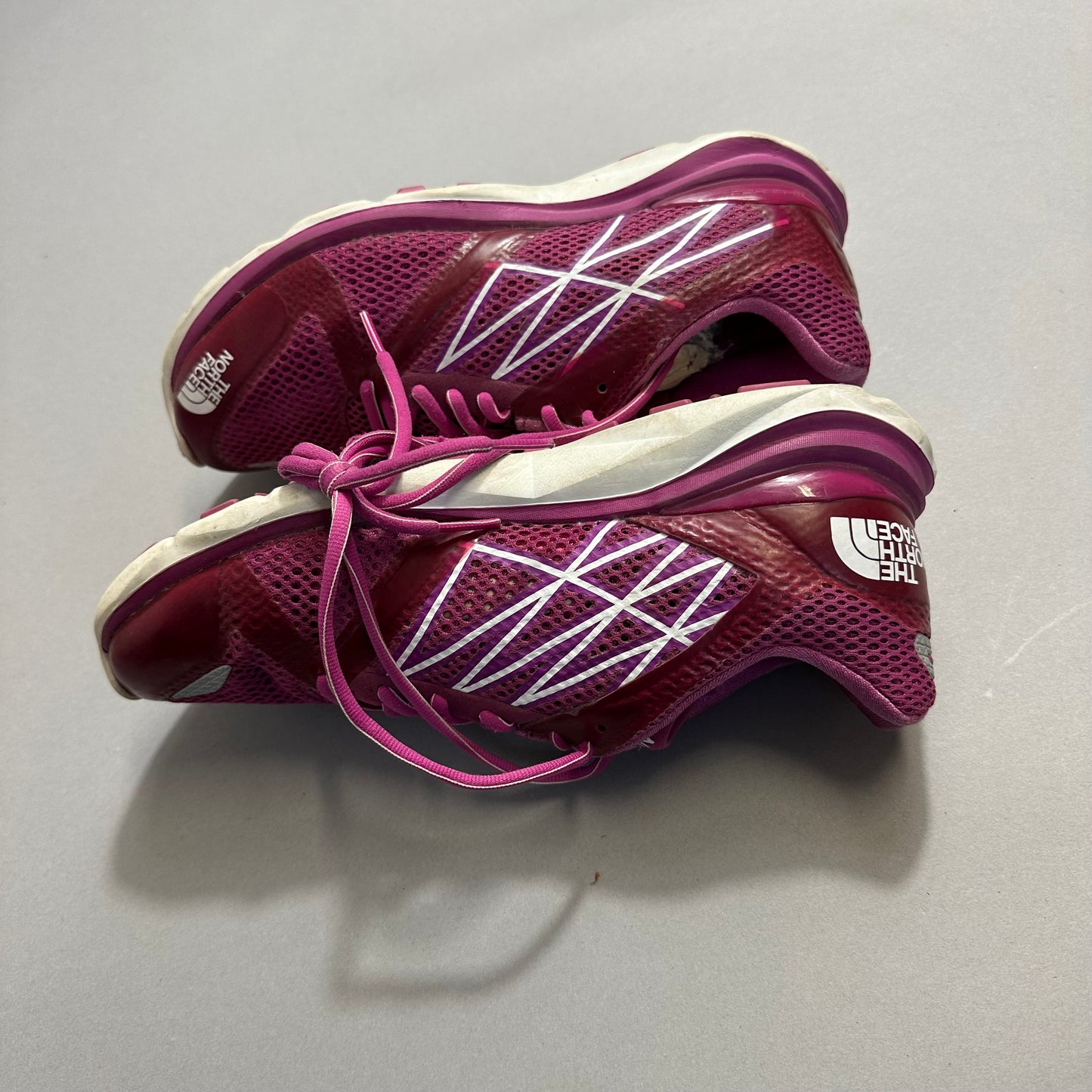 Pink athletic shoes with white patterns and laces on a gray surface.
