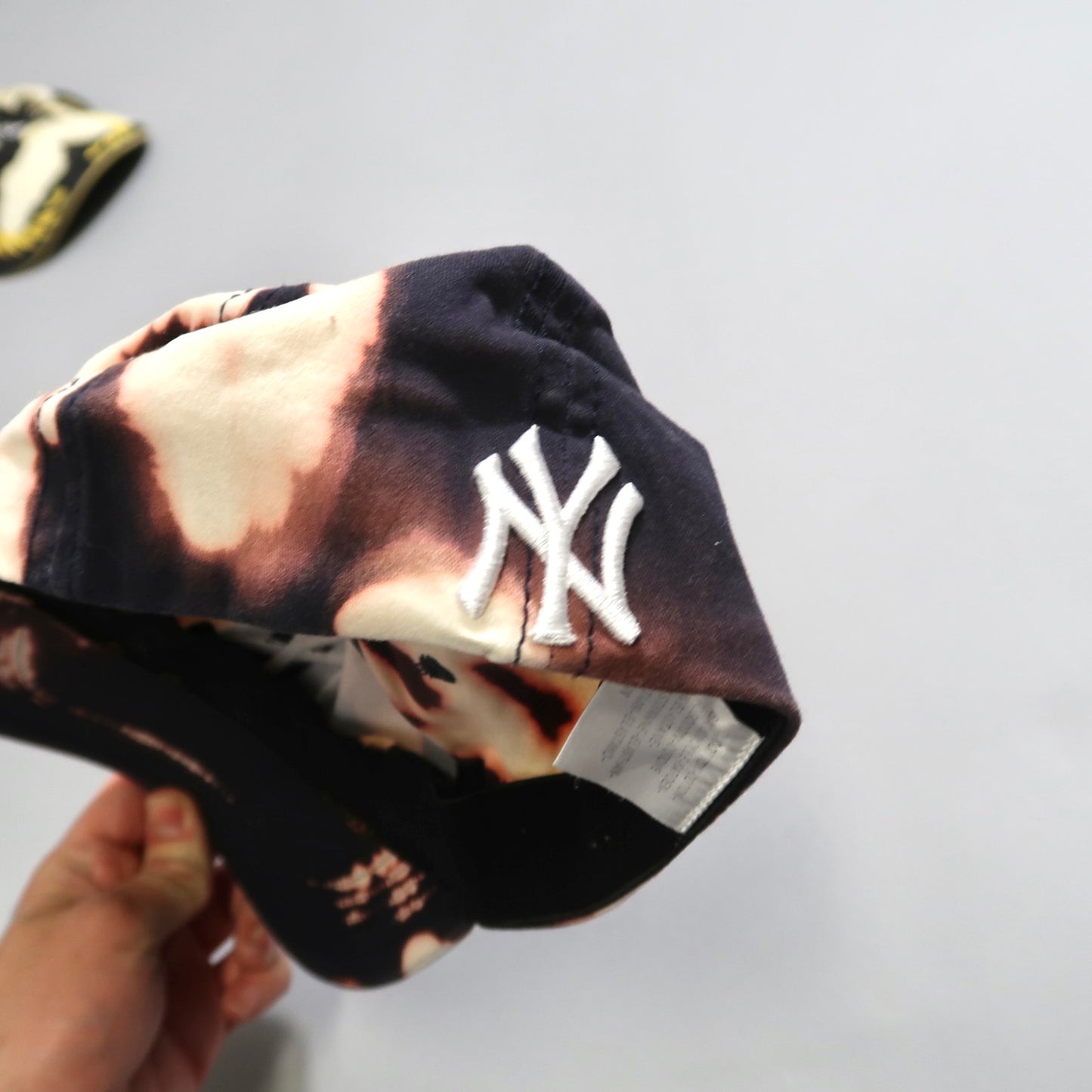 Tie-dye cap with nullNYnull logo being held in hand.