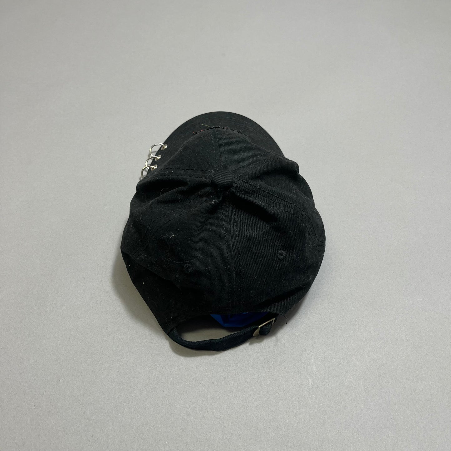 Black baseball cap with metal rings on a gray background.