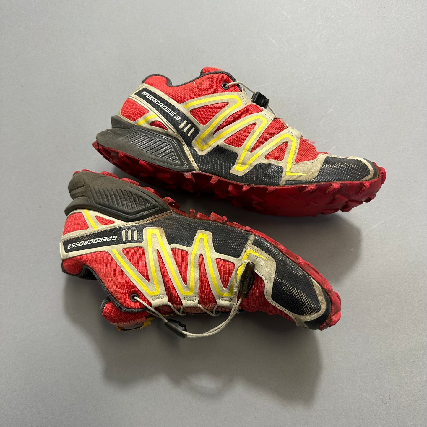 Red and yellow trail running shoes with rugged soles on a gray background.