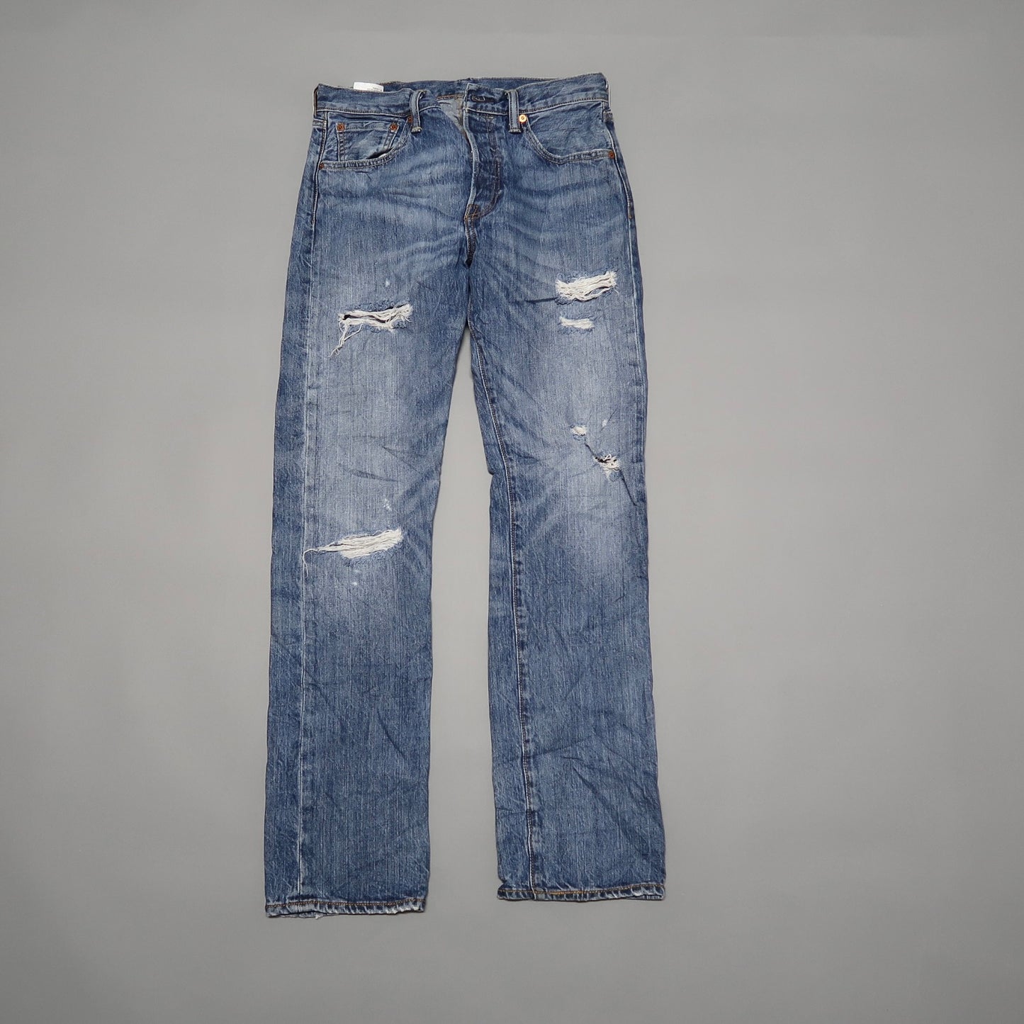 Distressed blue jeans with several rips, laid flat.