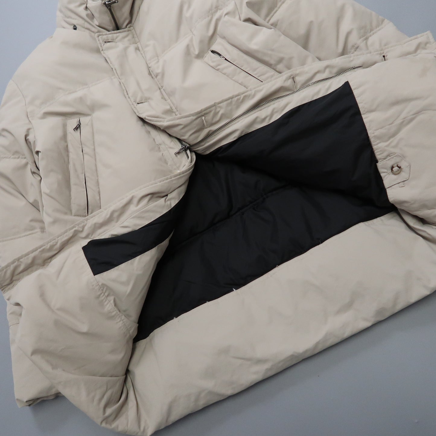 Beige puffer jacket with black lining, open to display interior pockets.