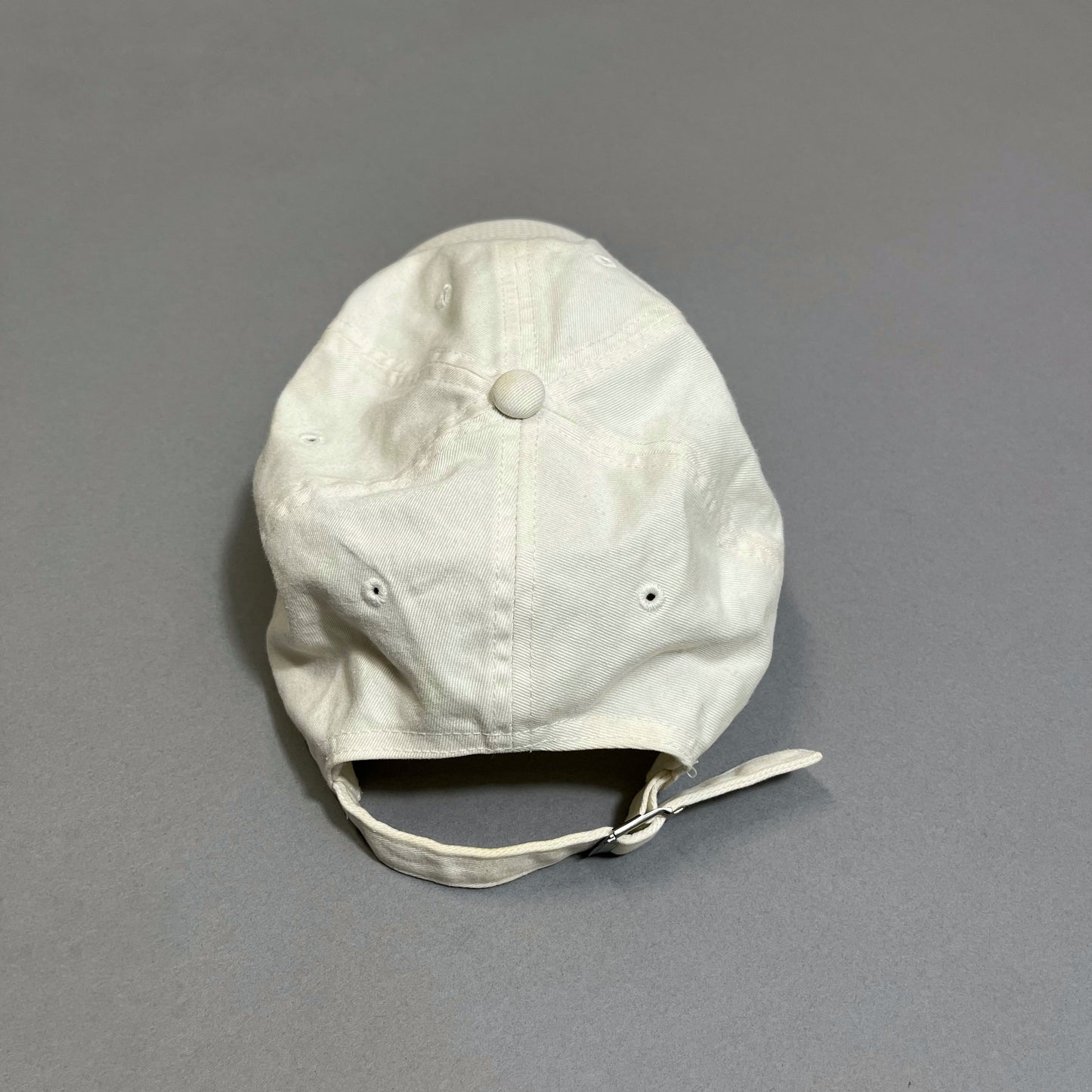 Back view of a white baseball cap on a gray surface.