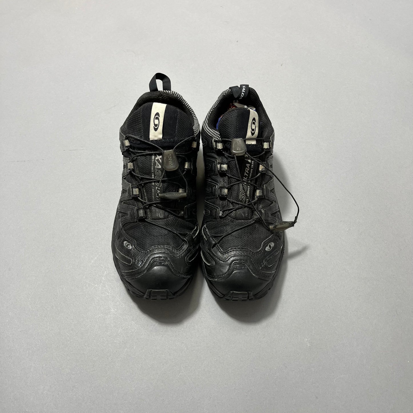 Pair of black trail running shoes on a gray surface.
