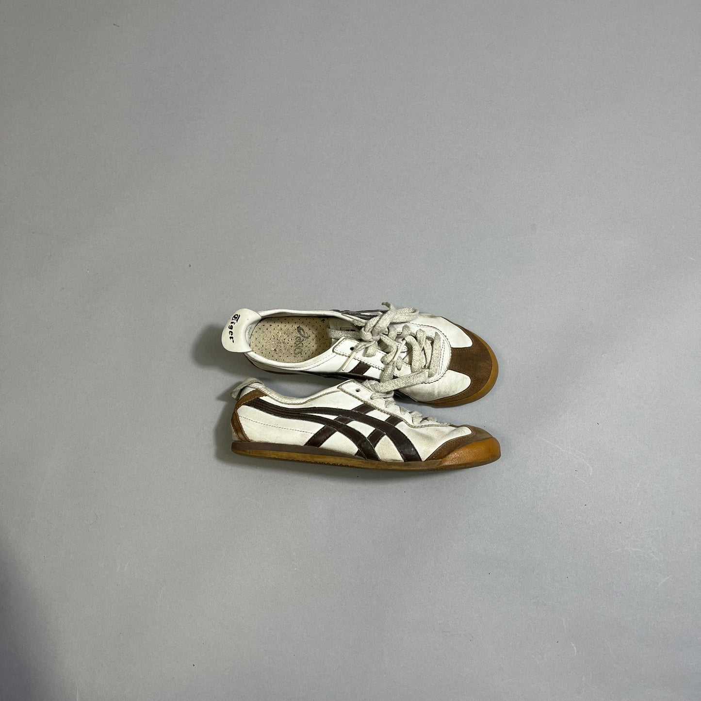 White and brown sneakers with black stripes on a neutral background.