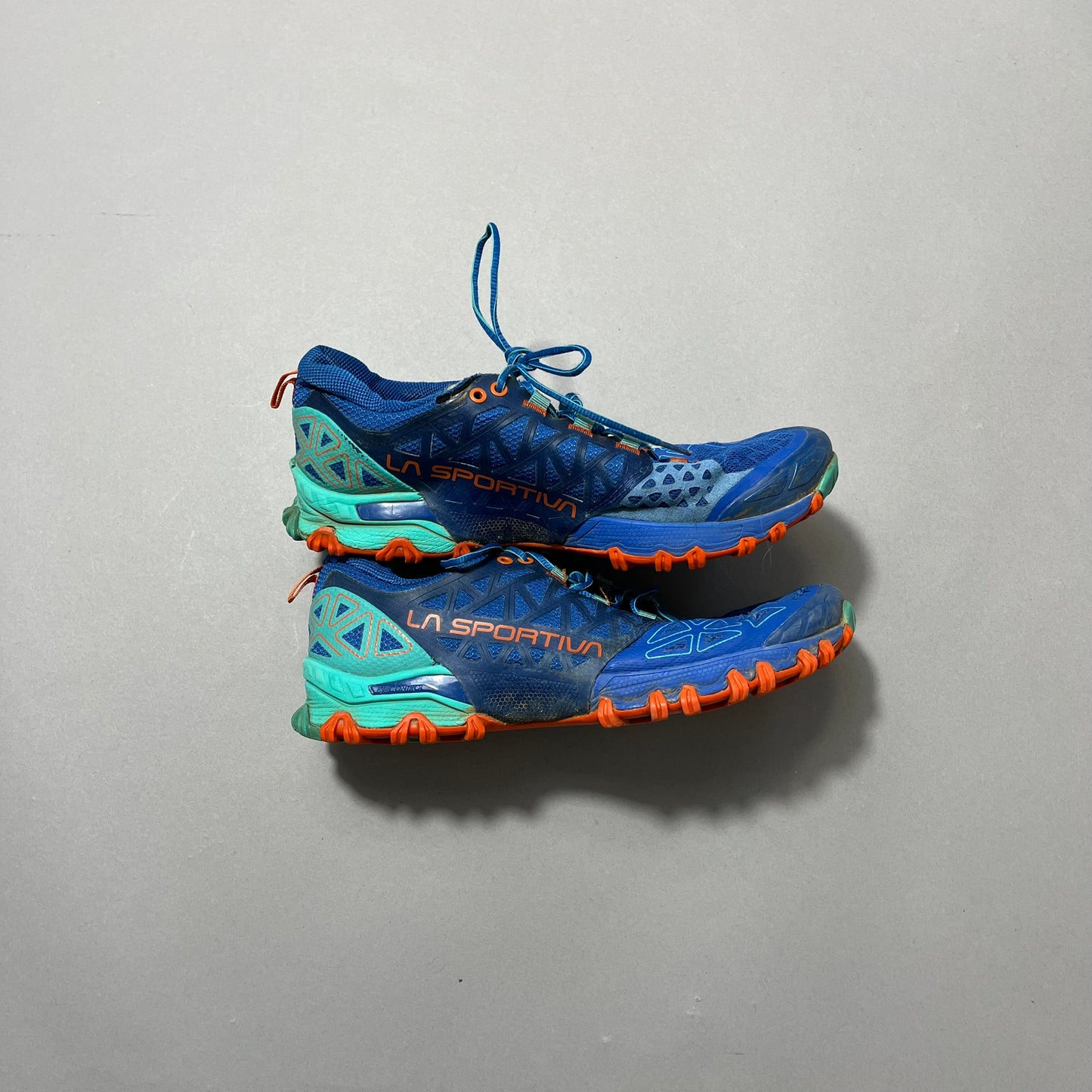 Blue and orange trail running shoes by La Sportiva on a gray background.