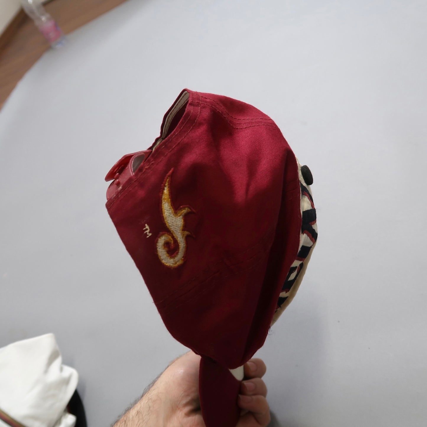 Red cap with embroidery held in hand, wooden floor background.