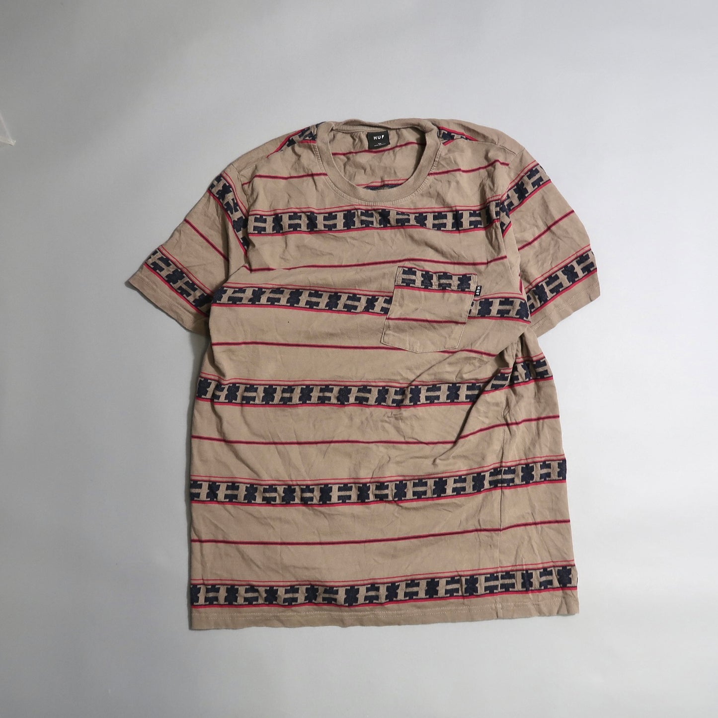 Beige T-shirt with red and navy geometric stripes on a flat surface.