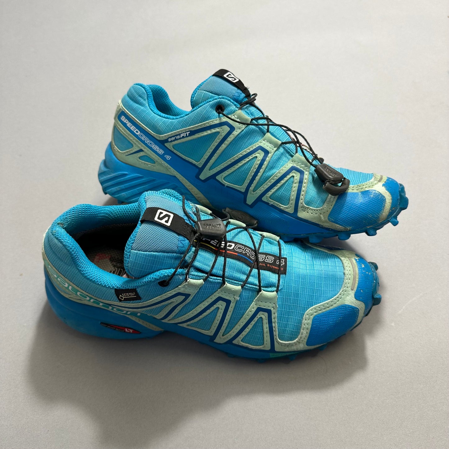 Blue trail running shoes with black laces on a gray background.