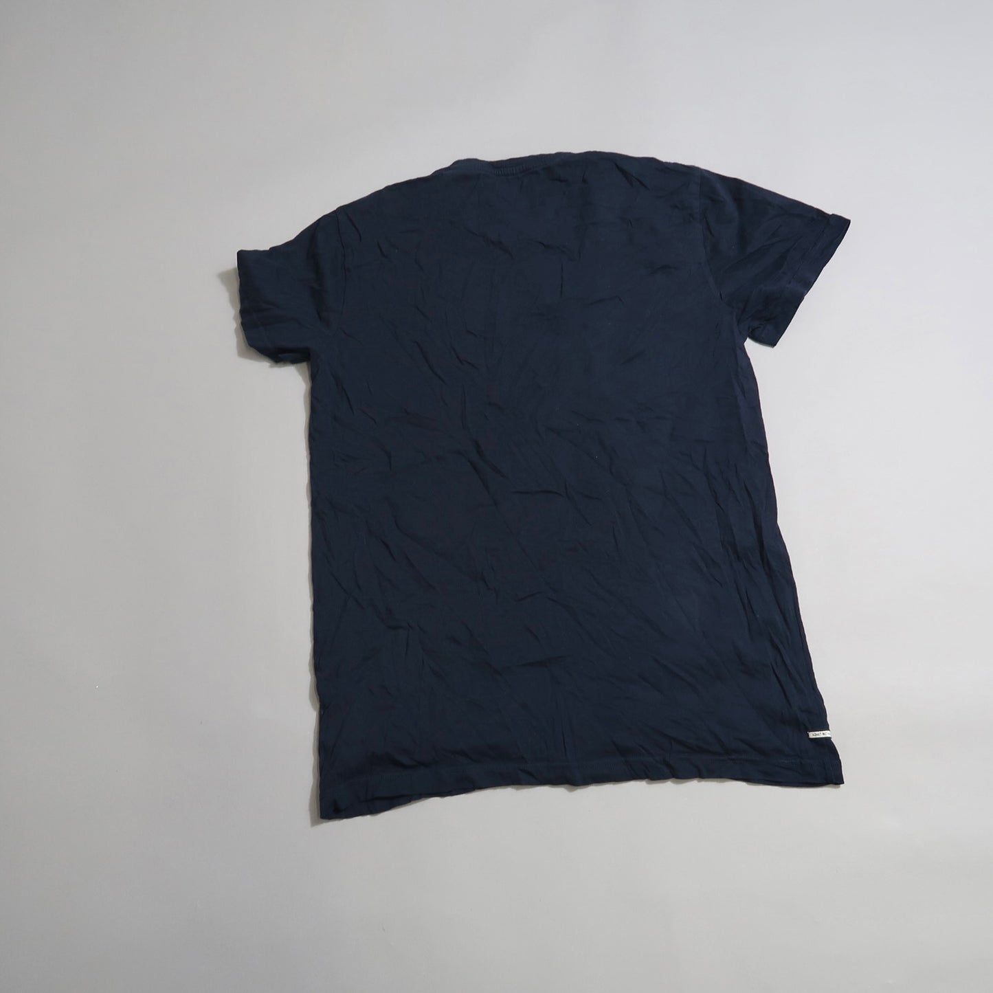 Wrinkled navy T-shirt laid flat on a plain surface.