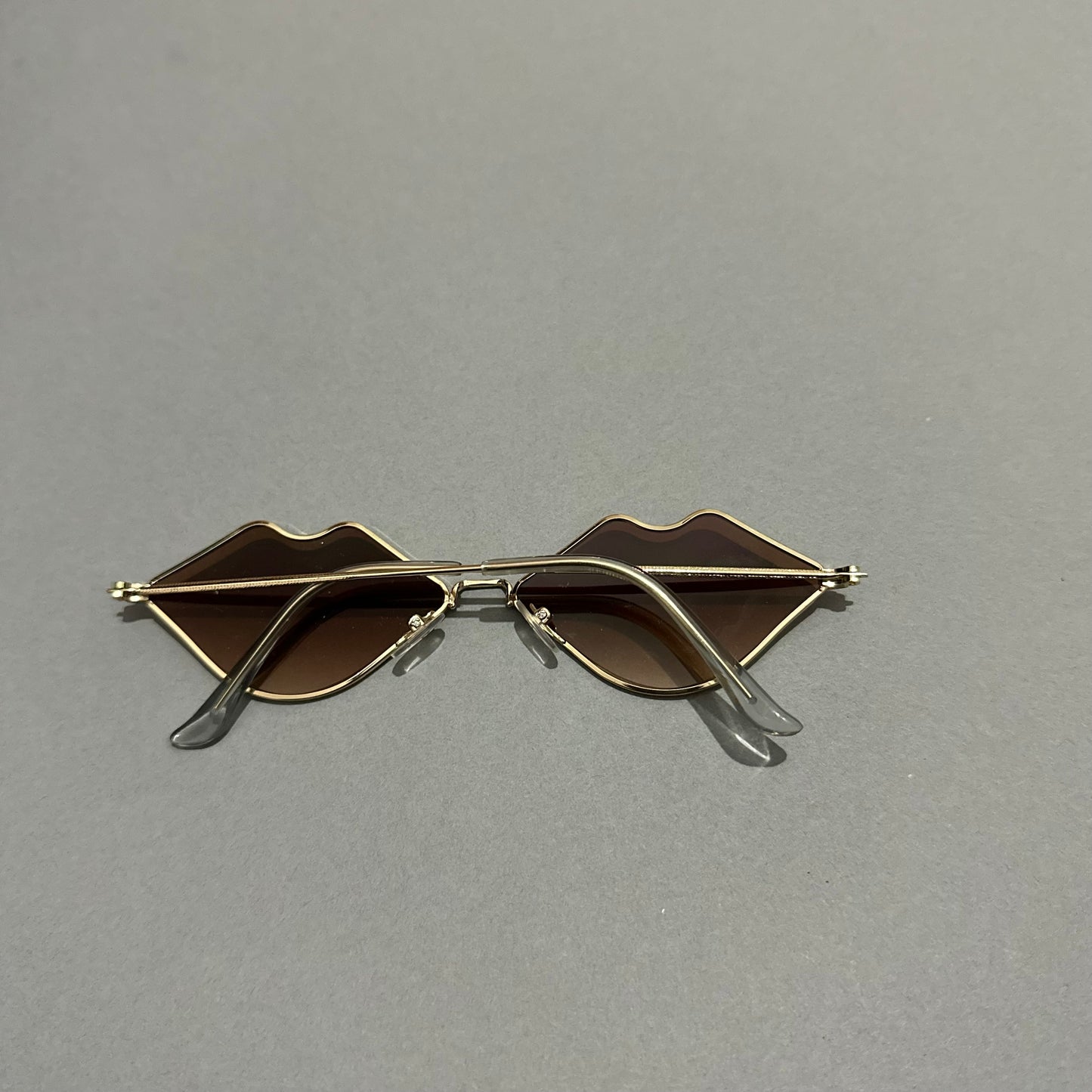 Lip-shaped sunglasses with gold rims on a gray background.