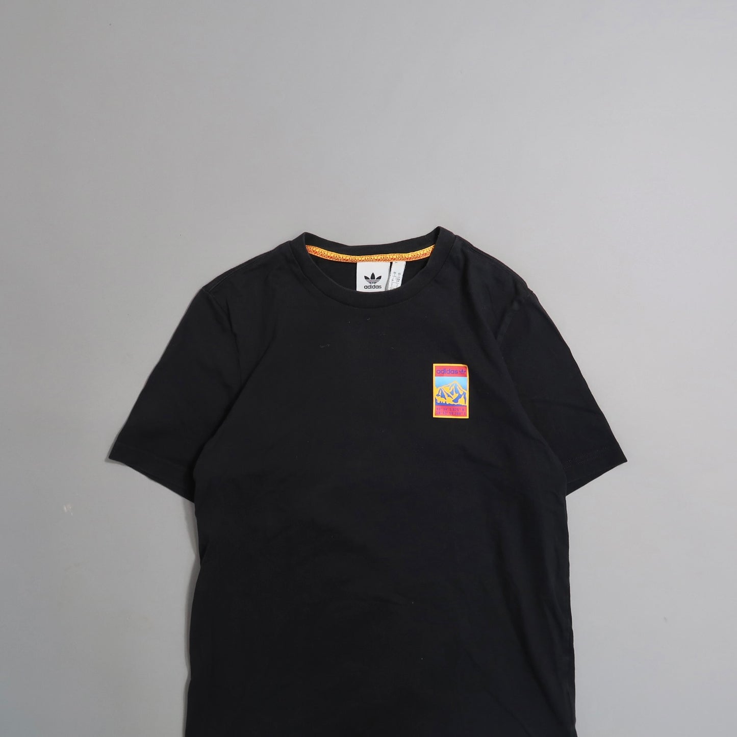 Black T-shirt with colorful chest logo displayed on gray background.