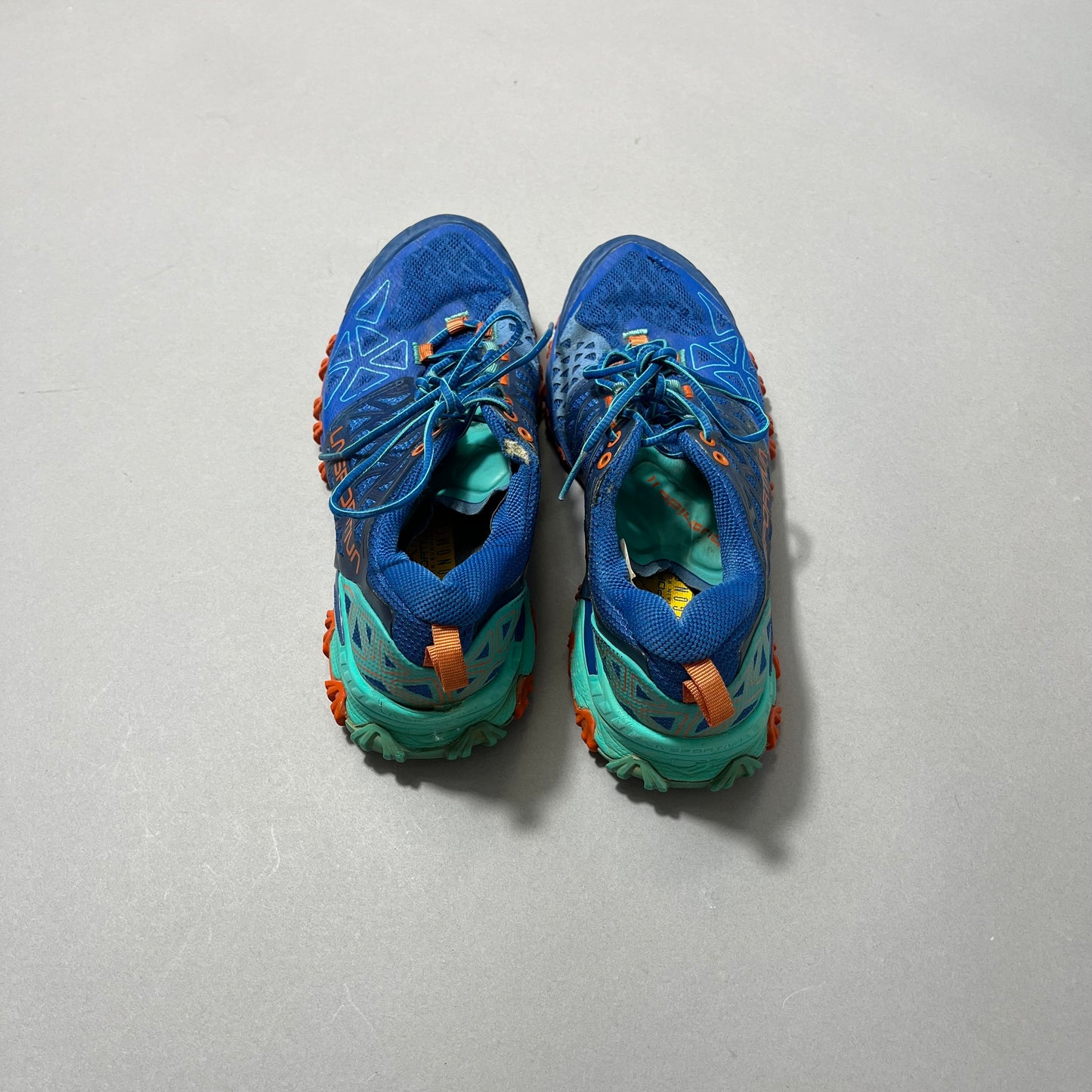 Blue and teal running shoes with orange accents on a gray floor.