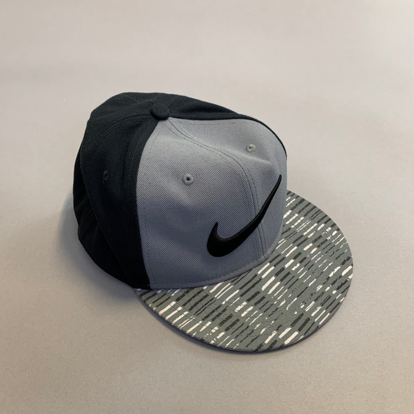Gray and black cap with patterned brim and swoosh logo.