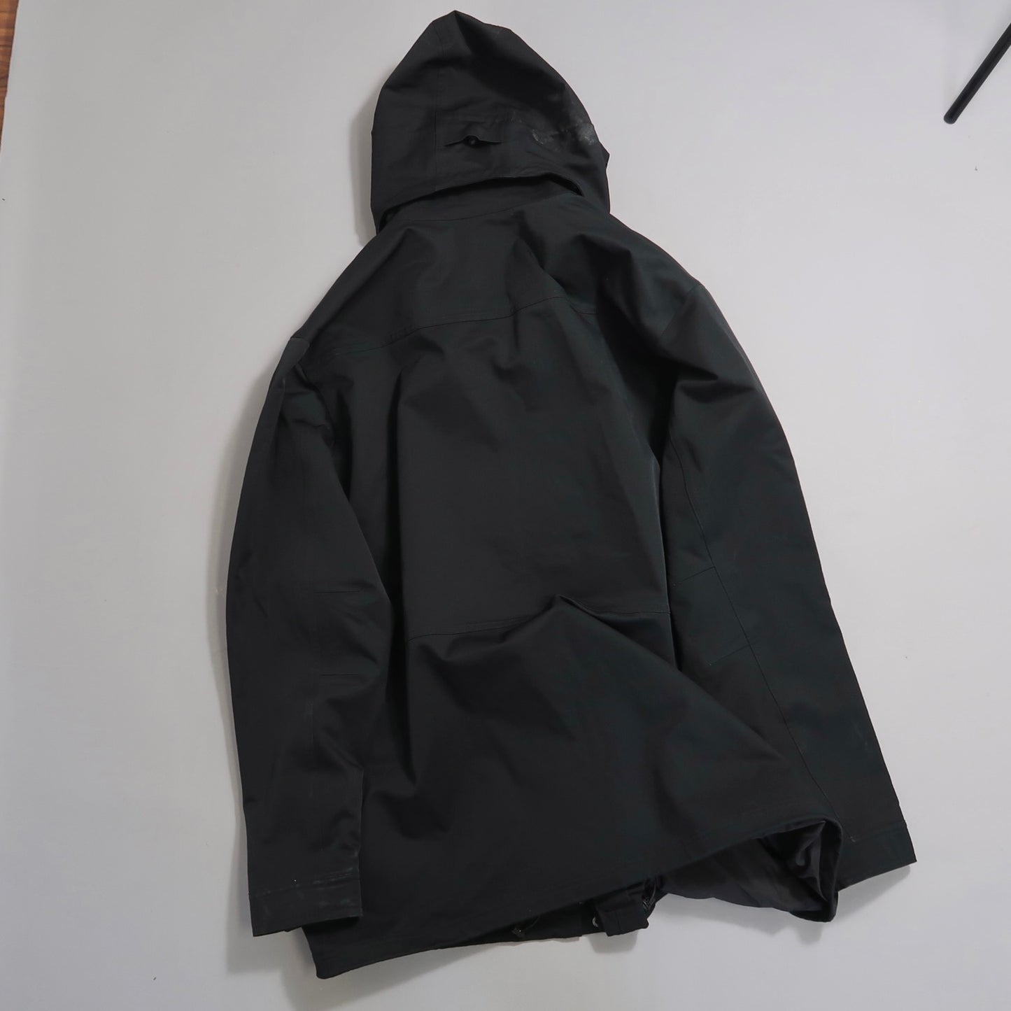 Black hooded jacket laid flat on white surface.