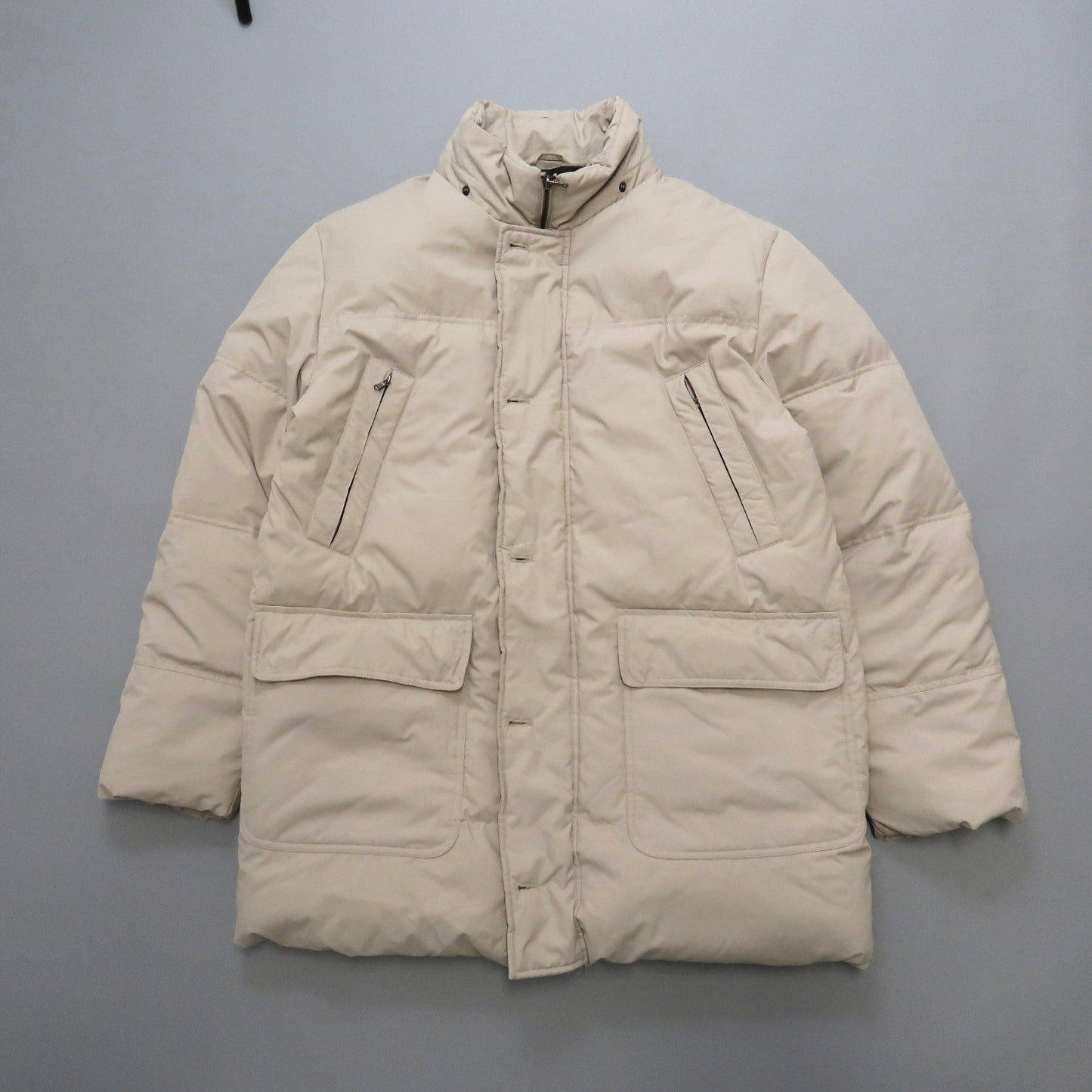Beige puffer jacket with multiple pockets on a gray background.