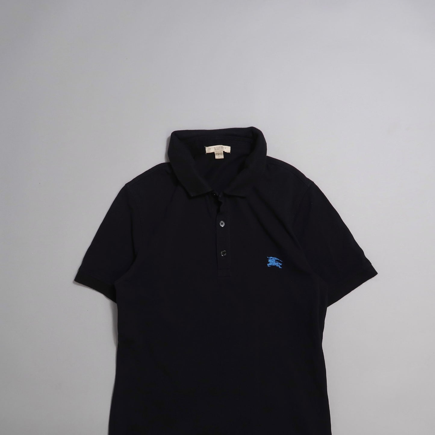 Black polo shirt with blue logo on chest, laid on a neutral background.