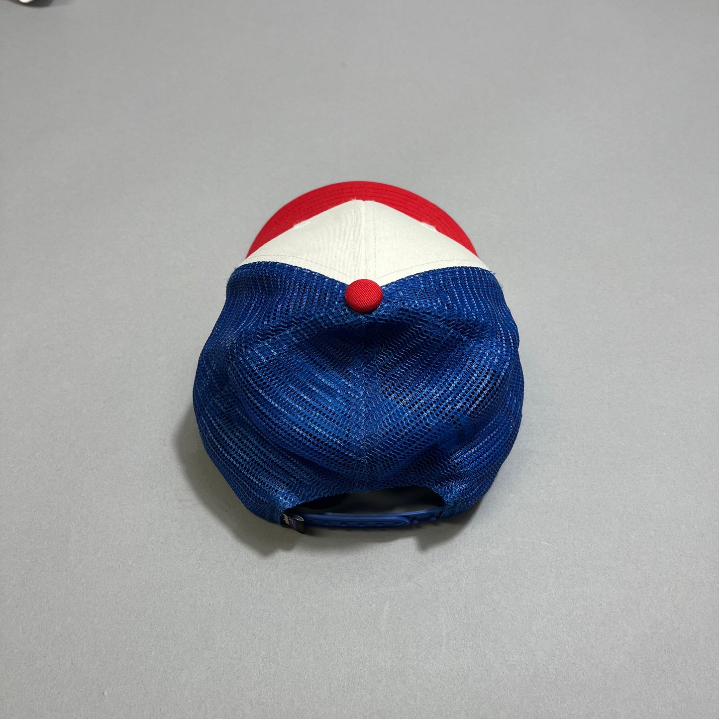 Red, white, and blue trucker cap on a gray surface, viewed from the back.