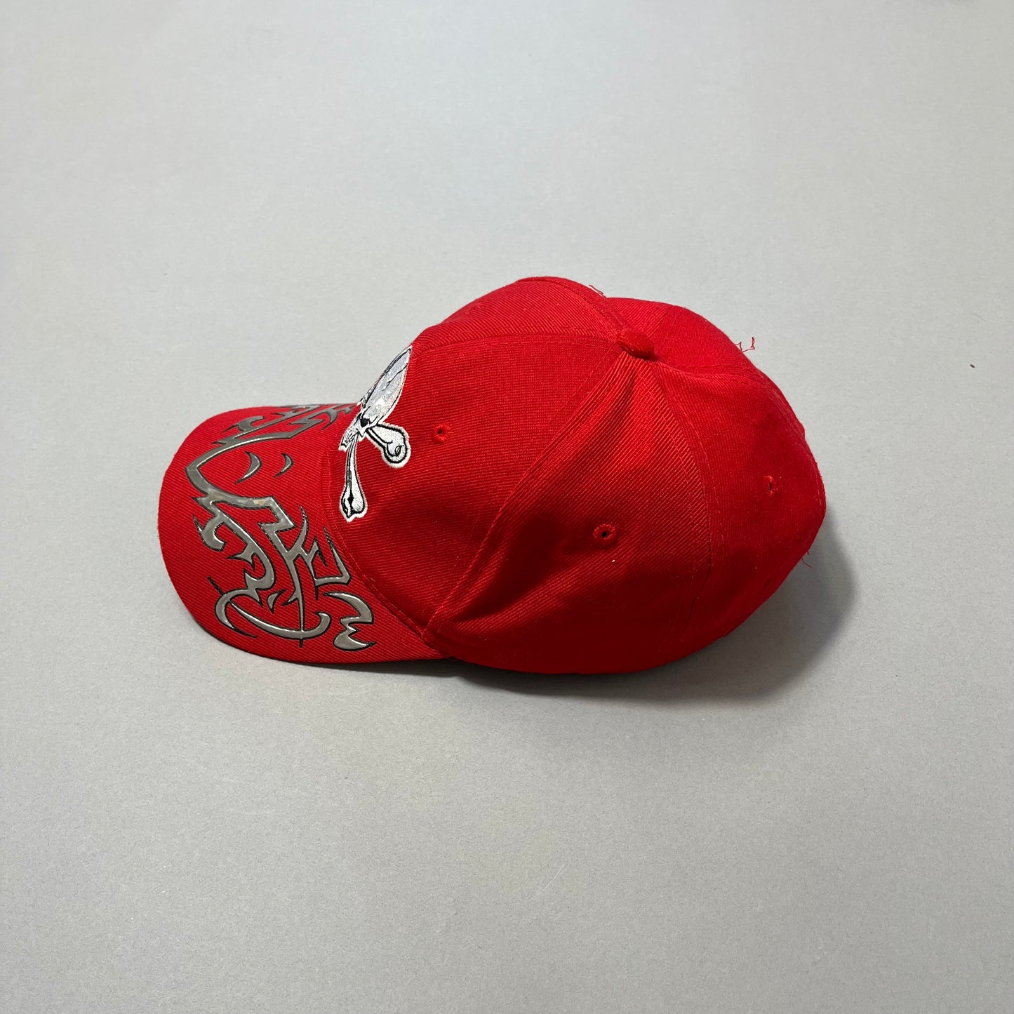 Red cap with skull and tribal design on brim, side view.