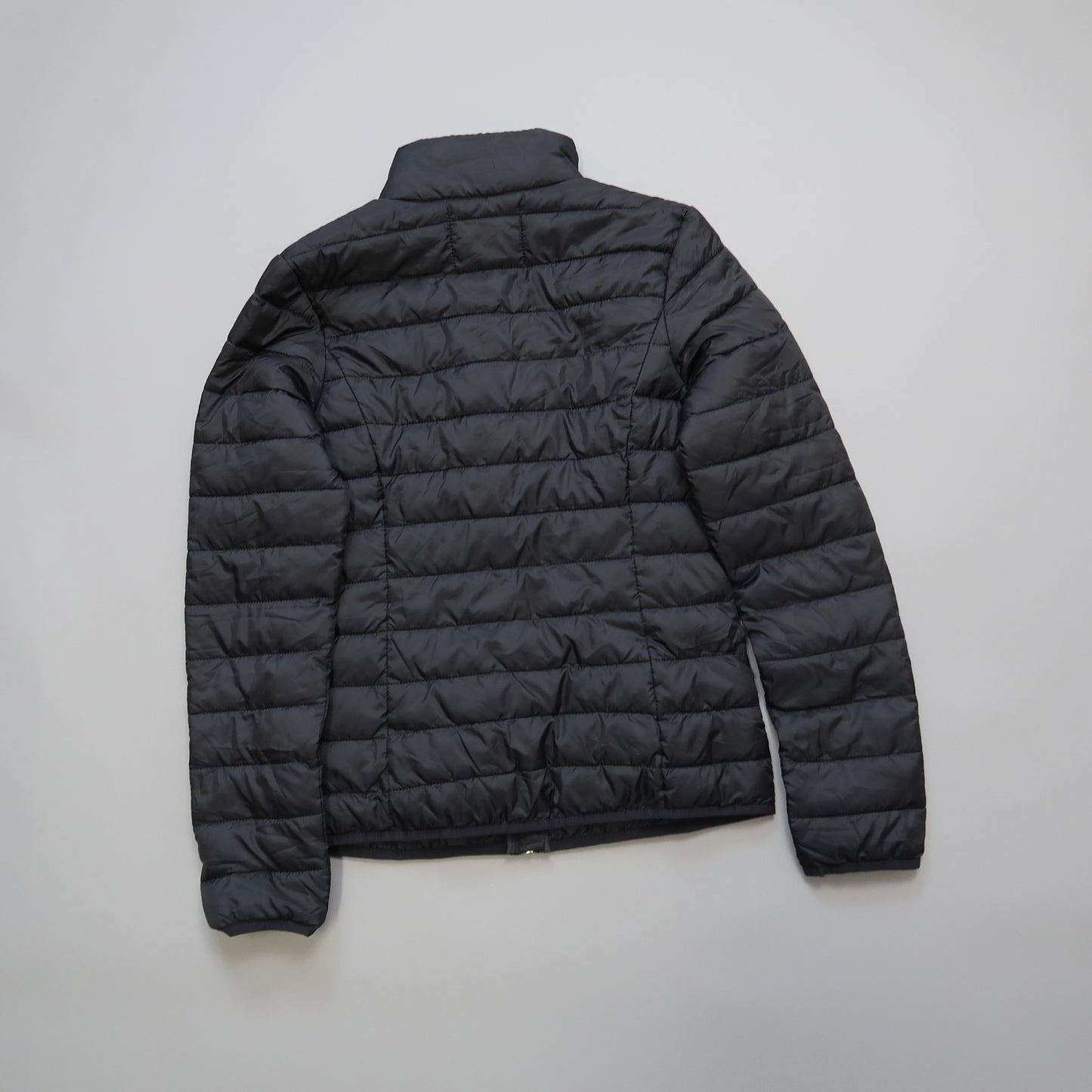 Black puffer jacket laid flat on a light background.
