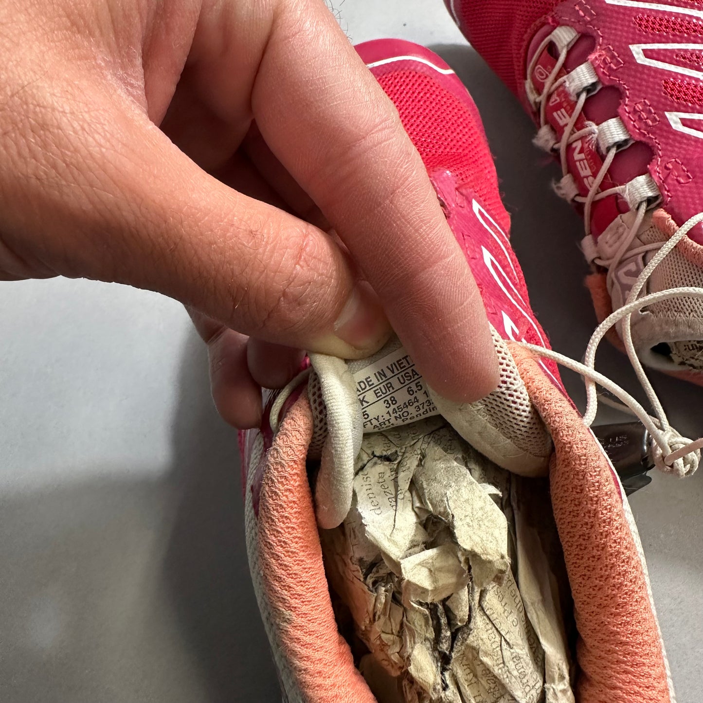 Hand holding a pink shoe tag, paper stuffed inside.