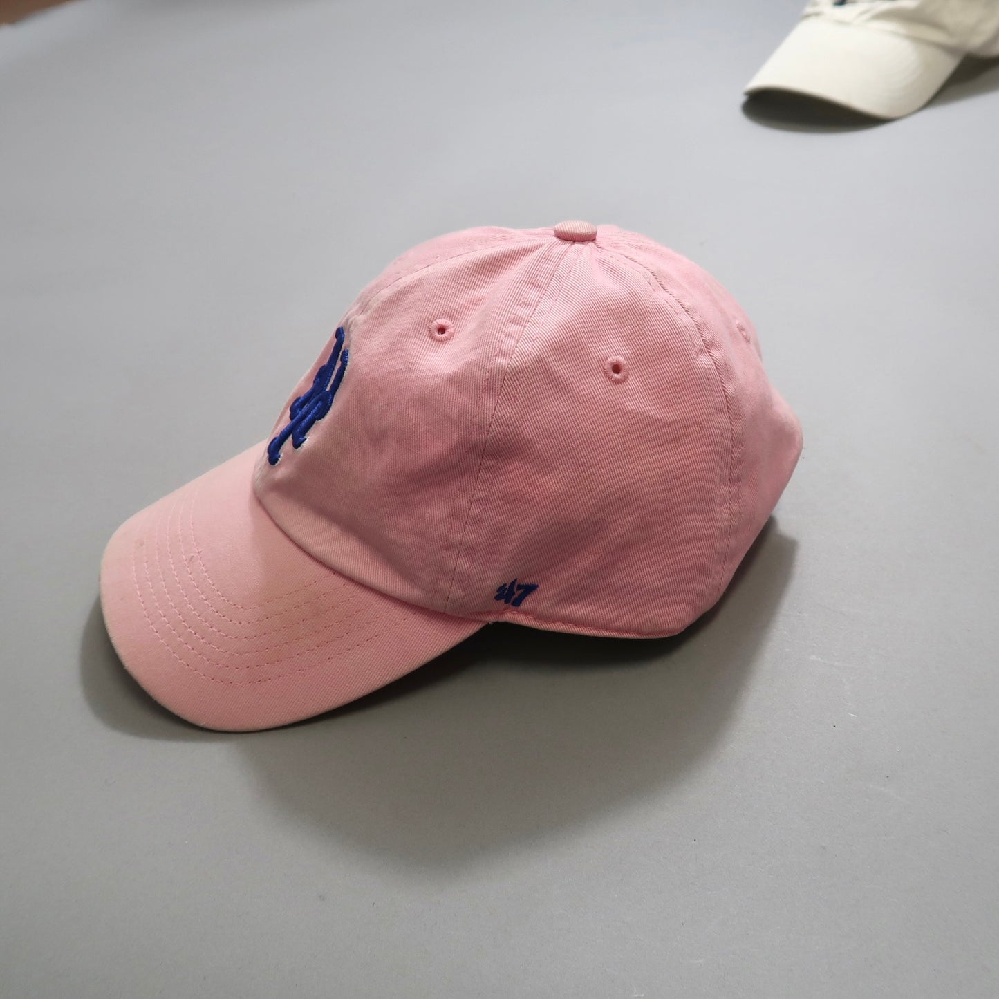 Pink baseball cap with a blue embroidered logo on a gray surface.