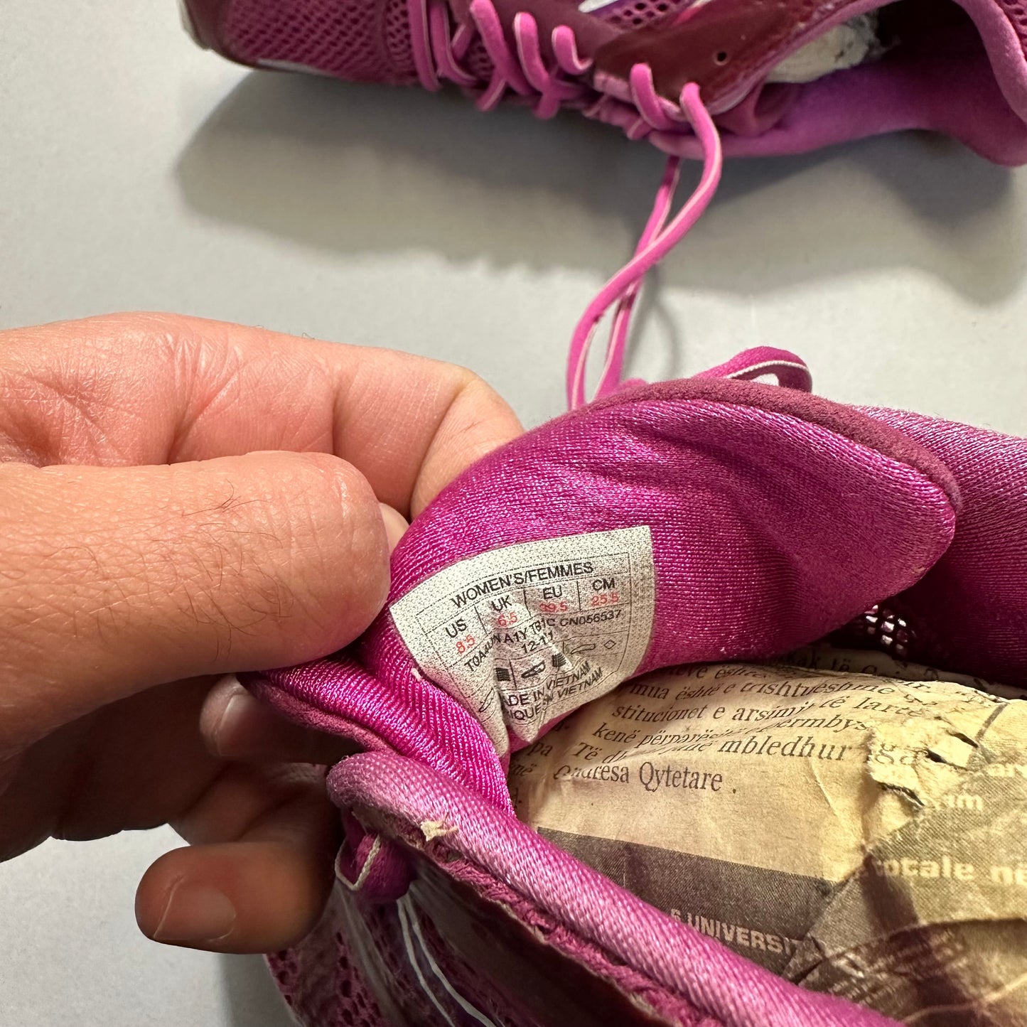 Hand holding a pink sneaker showing the size label inside.
