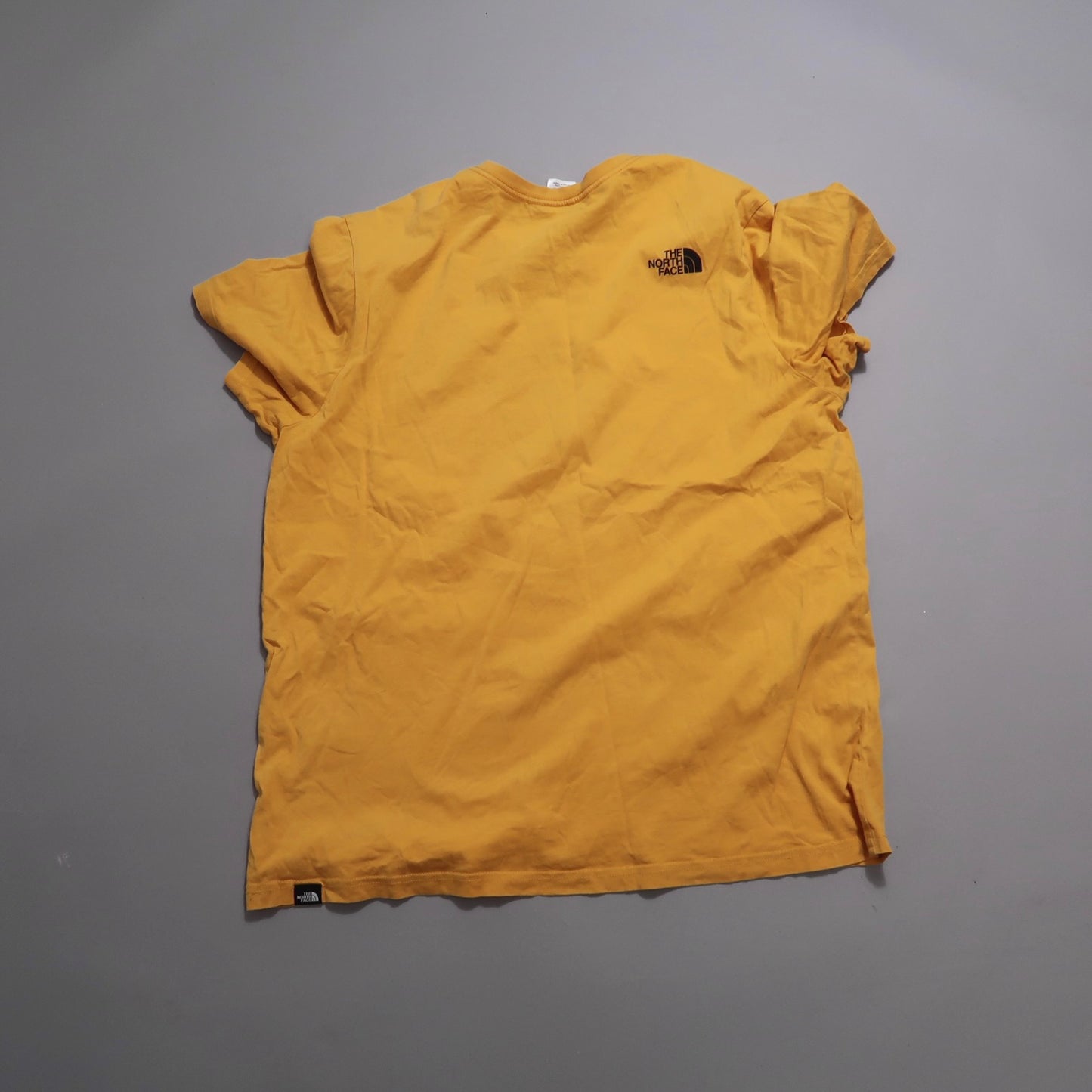 Yellow T-shirt with The North Face logo on the back, laid on a flat surface.