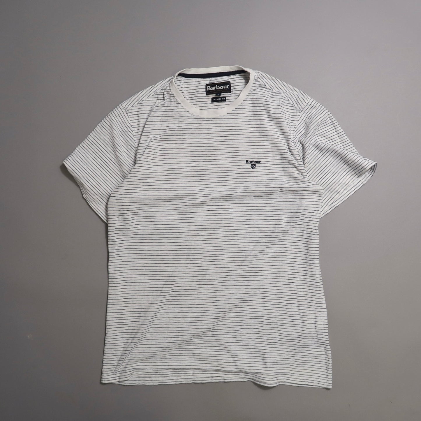 Striped white T-shirt with logo on chest, laid flat against a gray background.