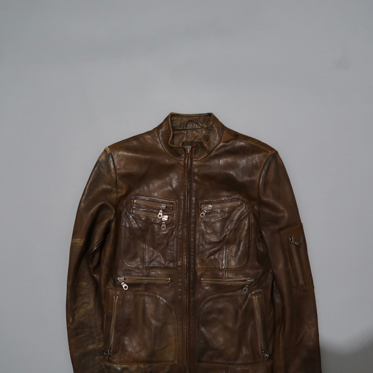 Brown leather jacket with multiple zippered pockets on gray background.