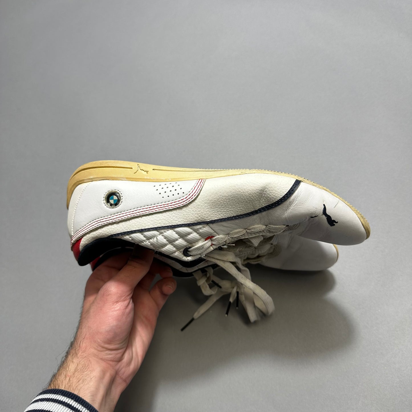 A person holds a white athletic shoe with a BMW and Puma logo.