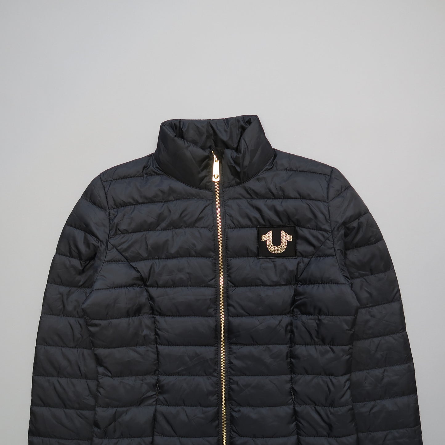 Black quilted jacket with gold zipper and logo on chest.