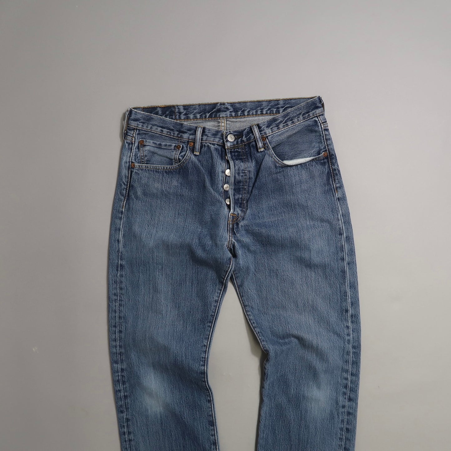 Blue jeans with exposed button fly on a neutral background.