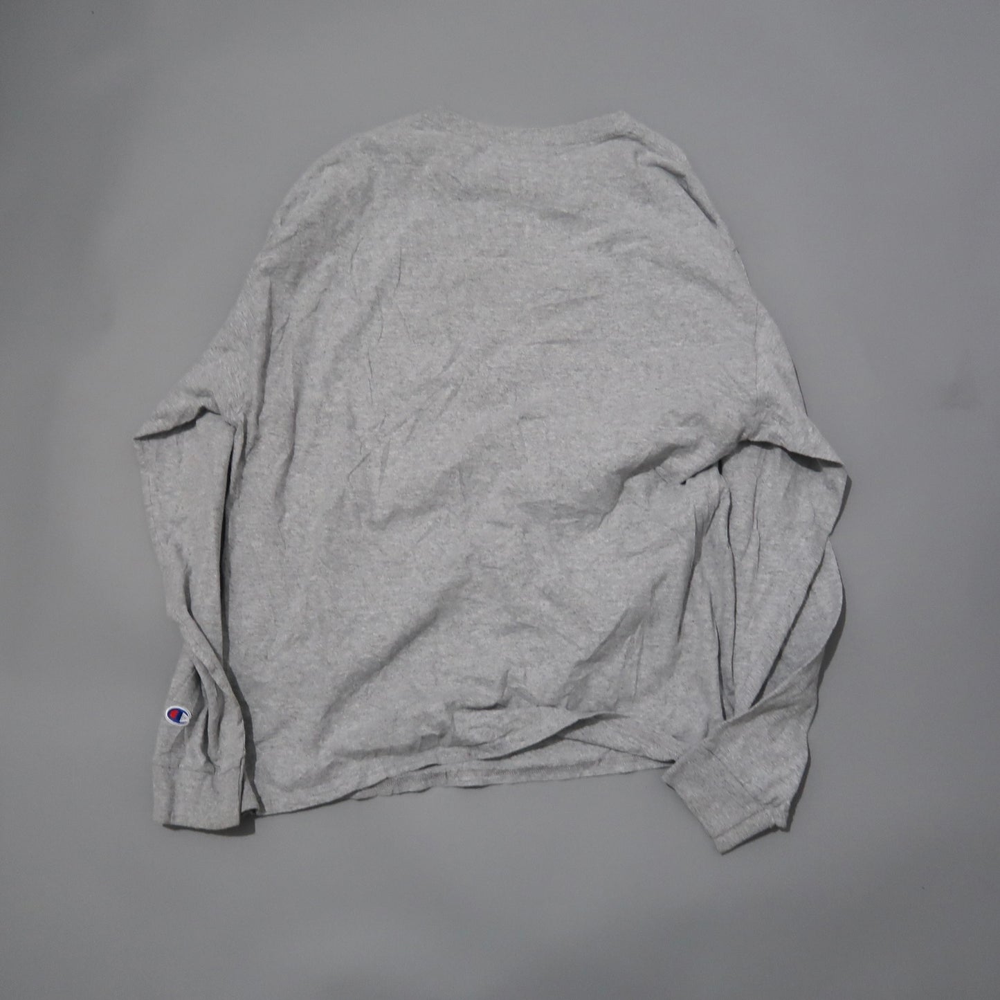 Gray long-sleeve shirt with small logo on cuff, laid on flat surface.