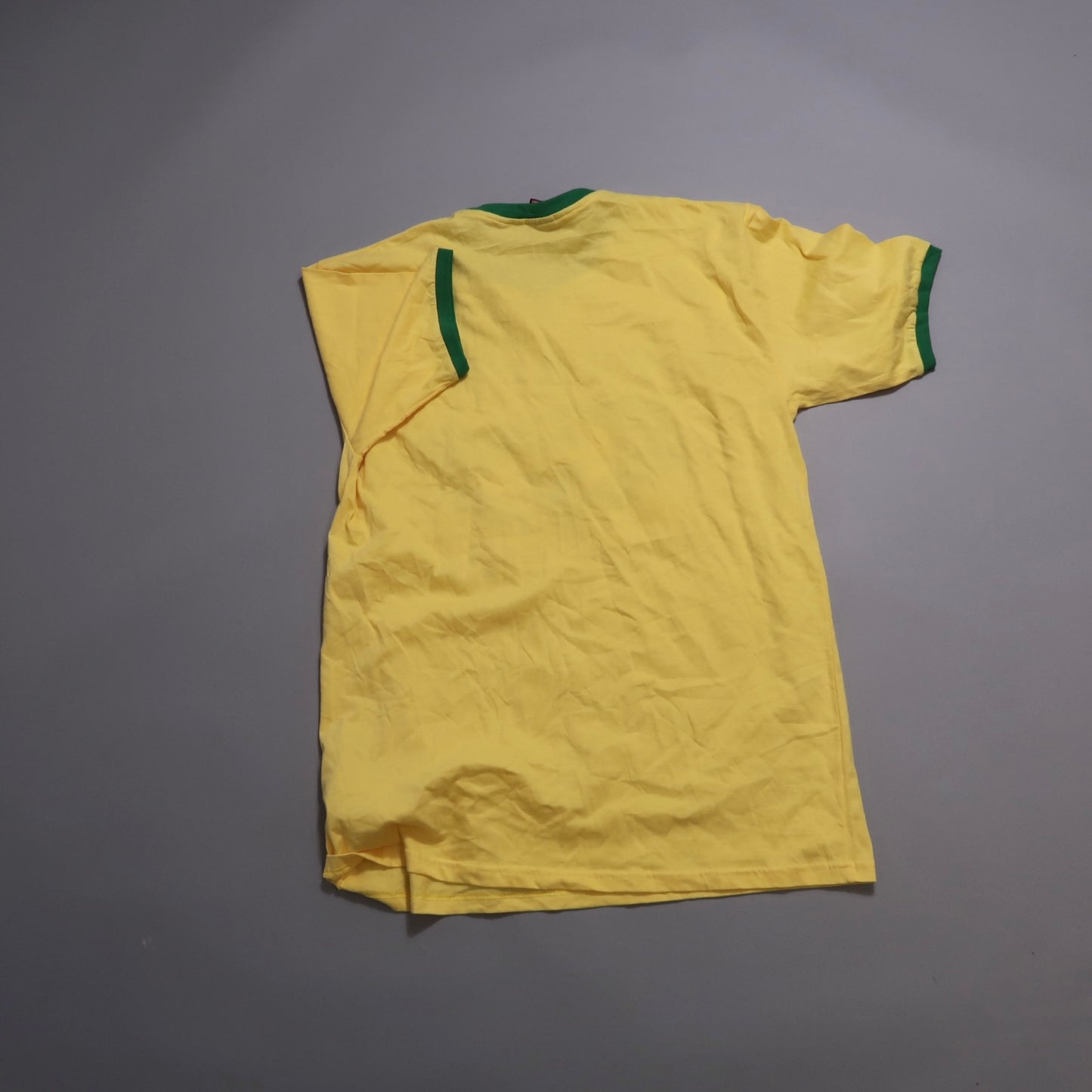 Yellow T-shirt with green trim, laid flat on a gray surface.
