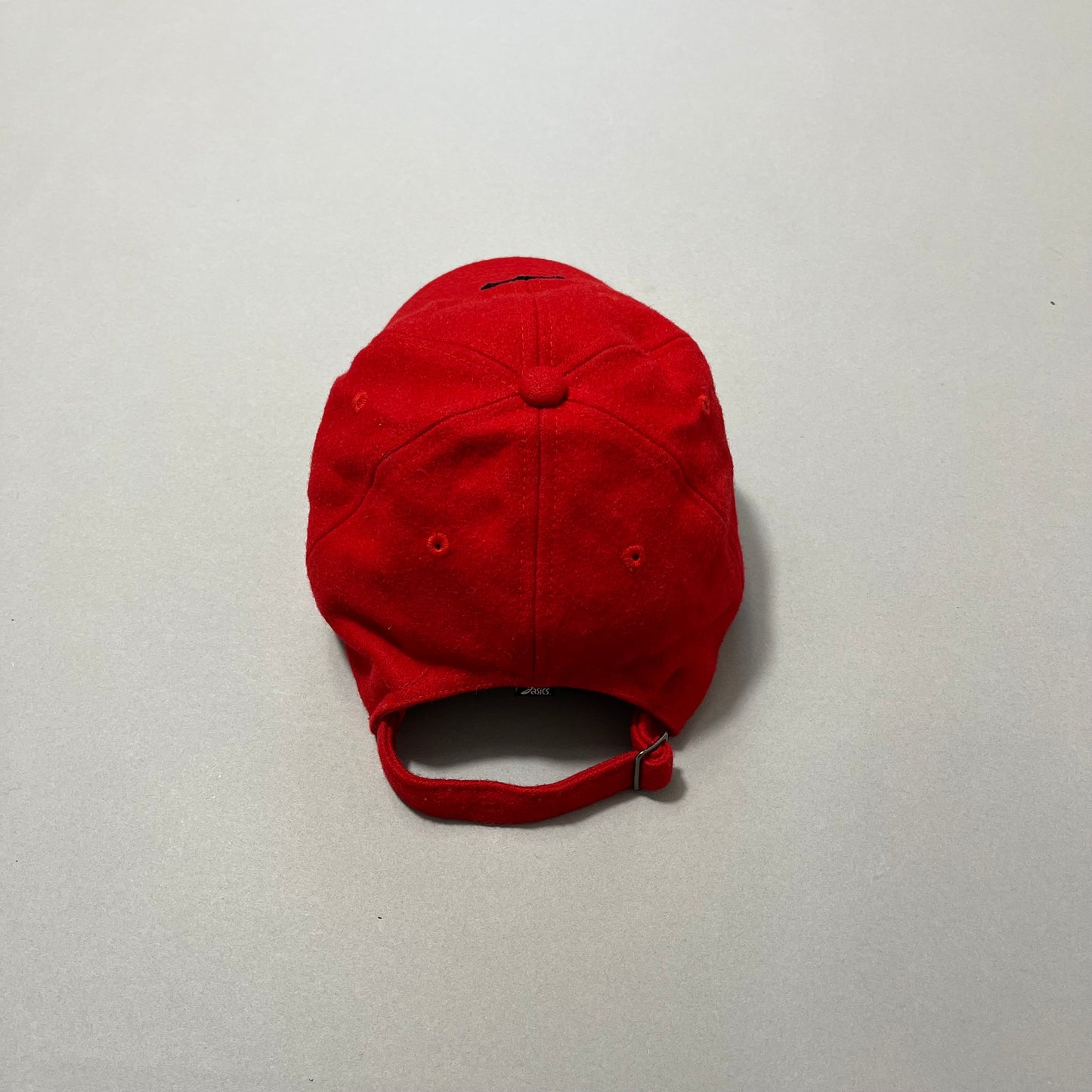 Red baseball cap with adjustable strap on plain background.