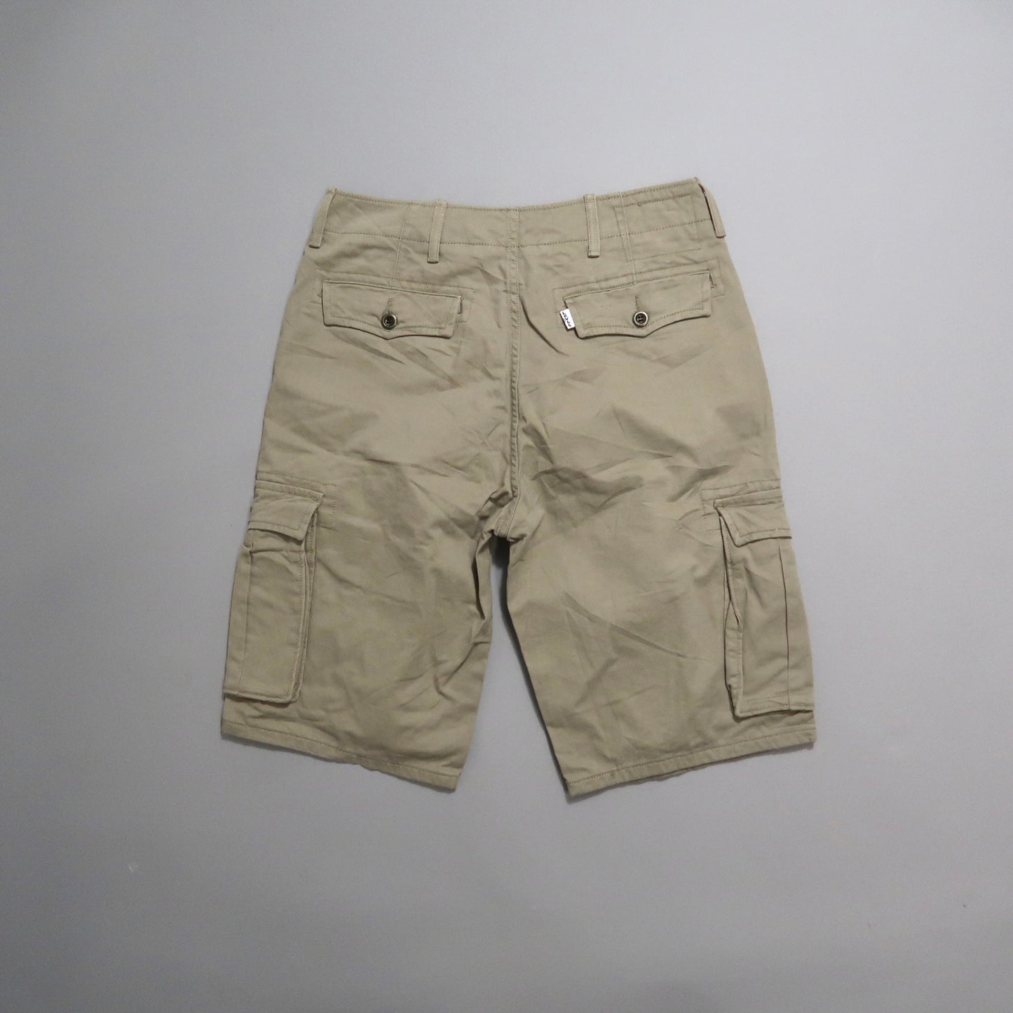 Back view of beige cargo shorts with pockets against gray background.