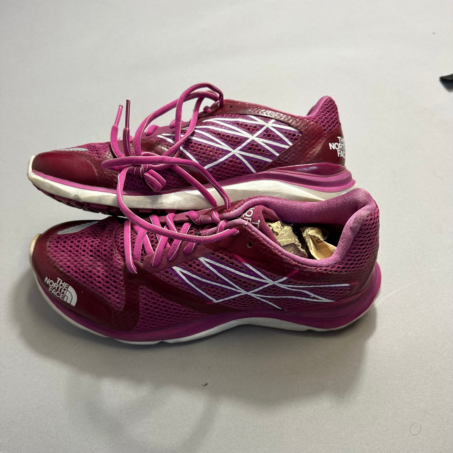 Pink athletic shoes with white accents and laces on a gray surface.