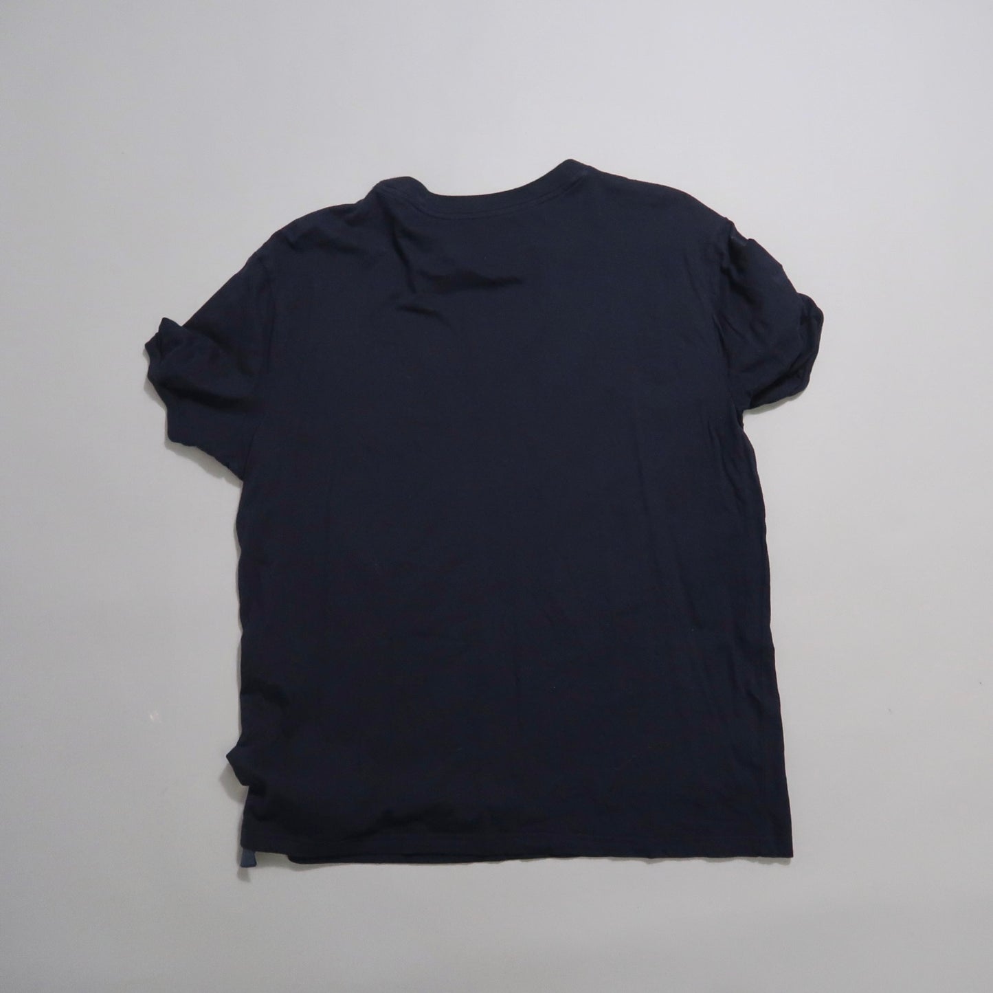 Back view of a plain black T-shirt on a gray background.
