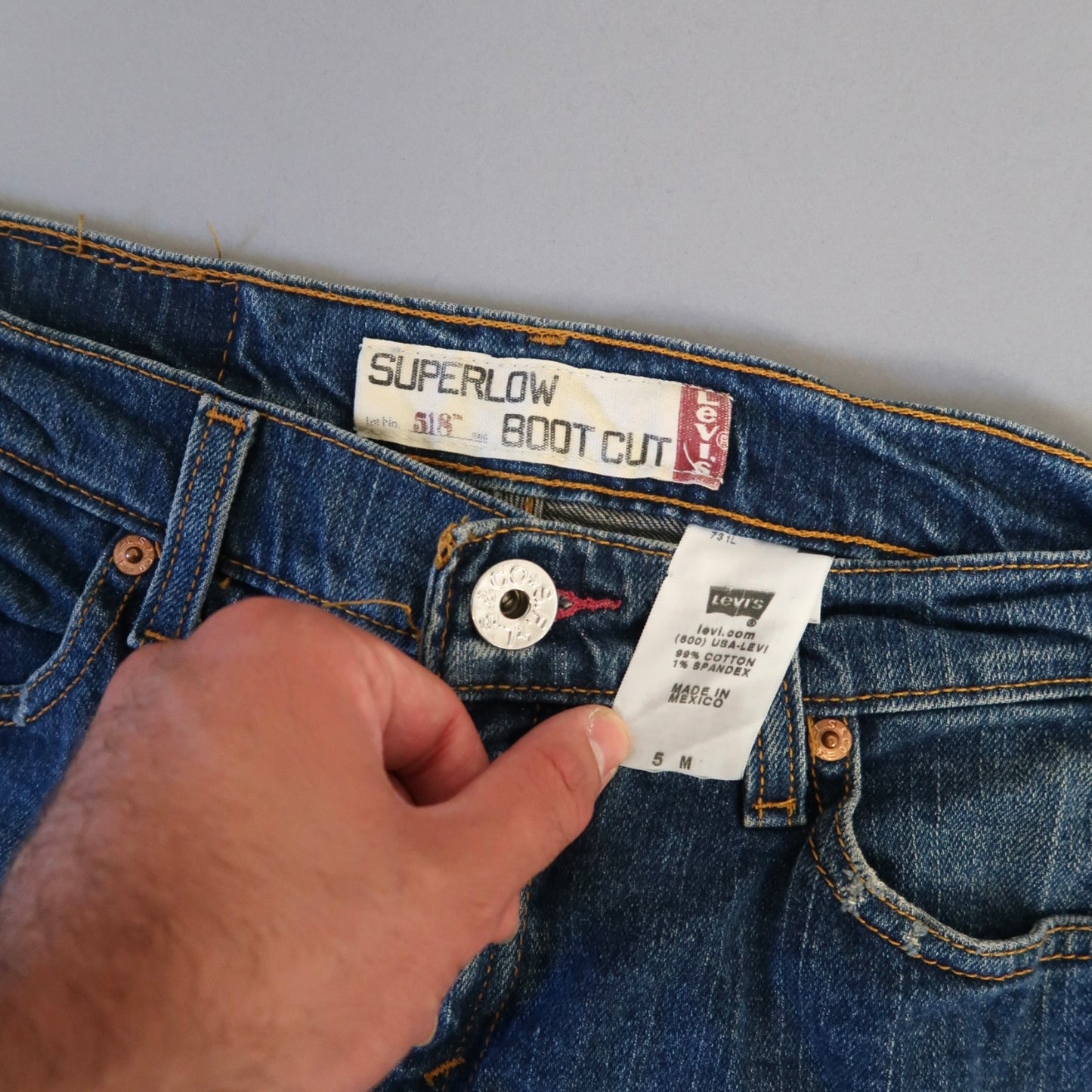 Hand holding Levi's Superlow Boot Cut jeans with visible tags.