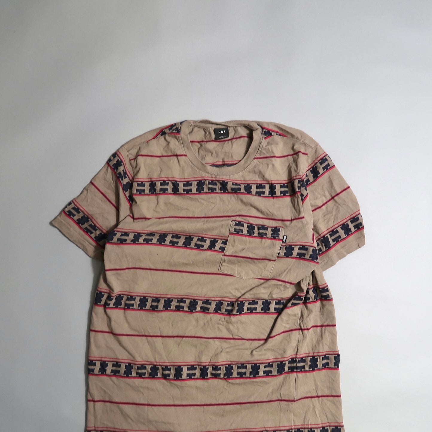 Beige T-shirt with red and patterned black stripes, pocket on chest.