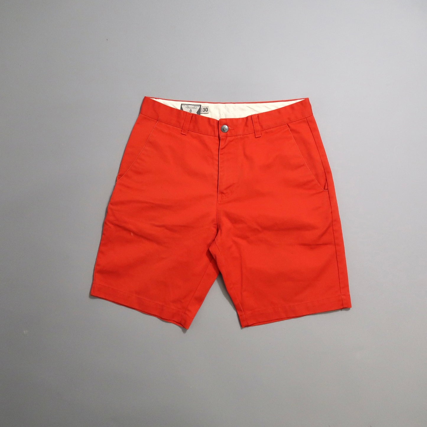 Bright red shorts with button closure on a plain gray background.