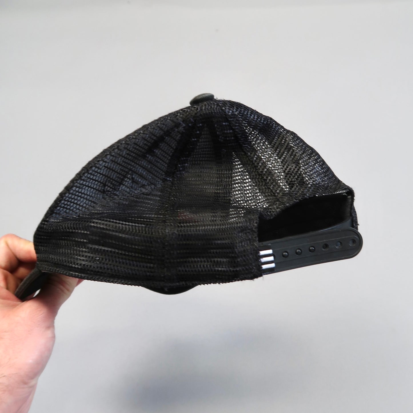 Hand holding a black mesh trucker cap with an adjustable strap.