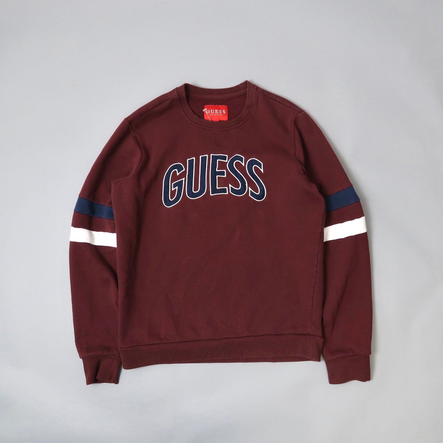Maroon sweatshirt with nullGUESSnull text and striped sleeves.