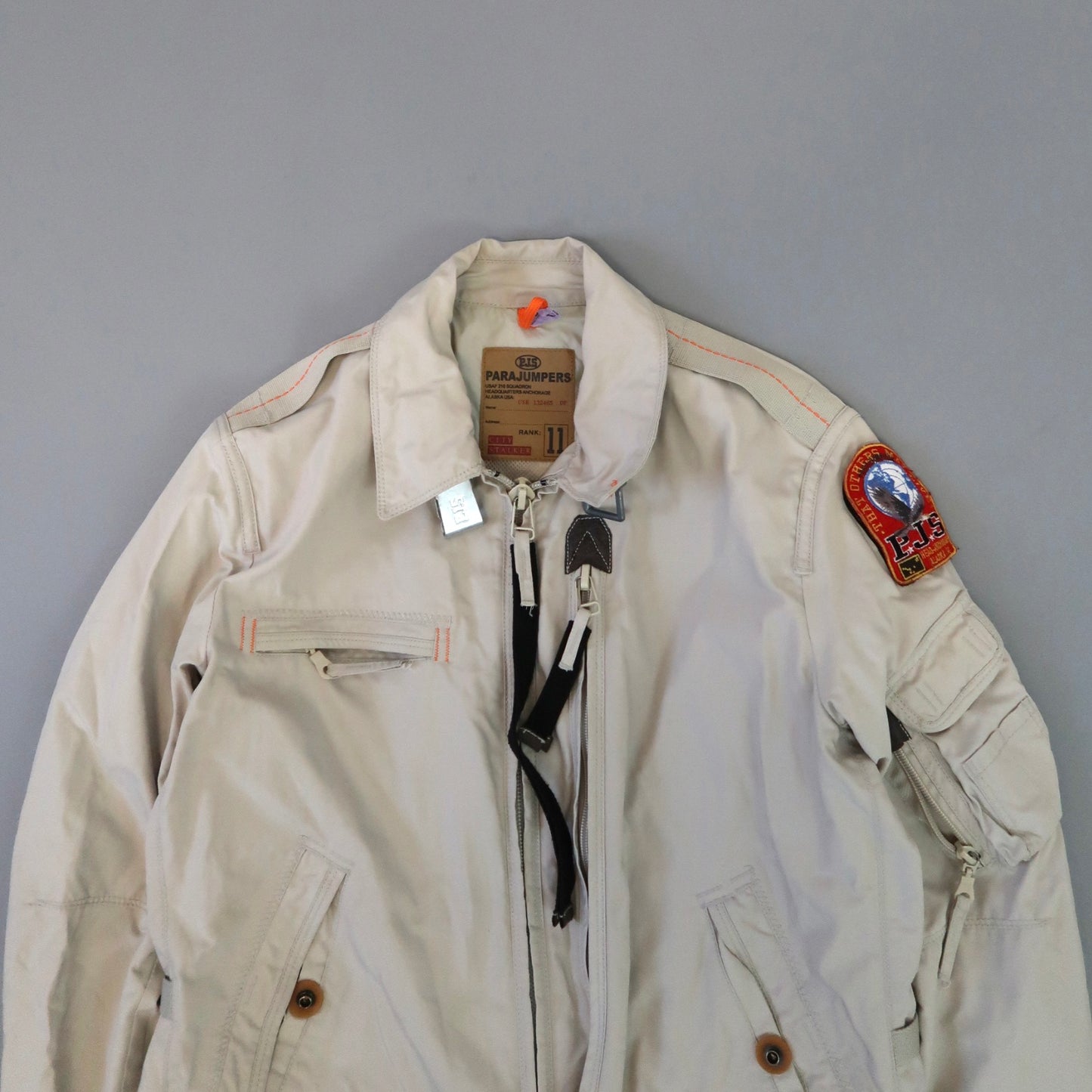 Beige Parajumpers jacket with patches and orange accents.