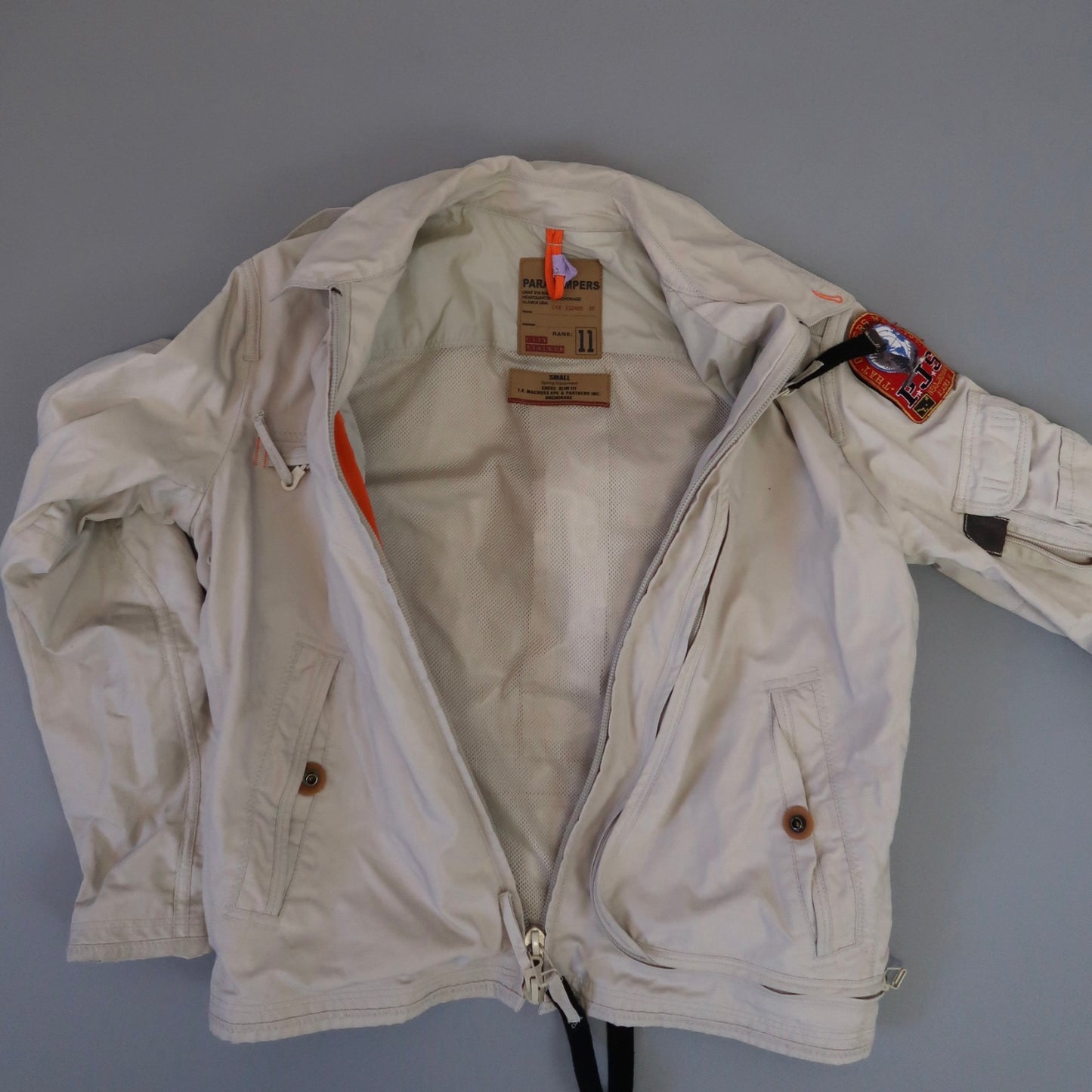 Light beige jacket with patches and tags on a grey background.