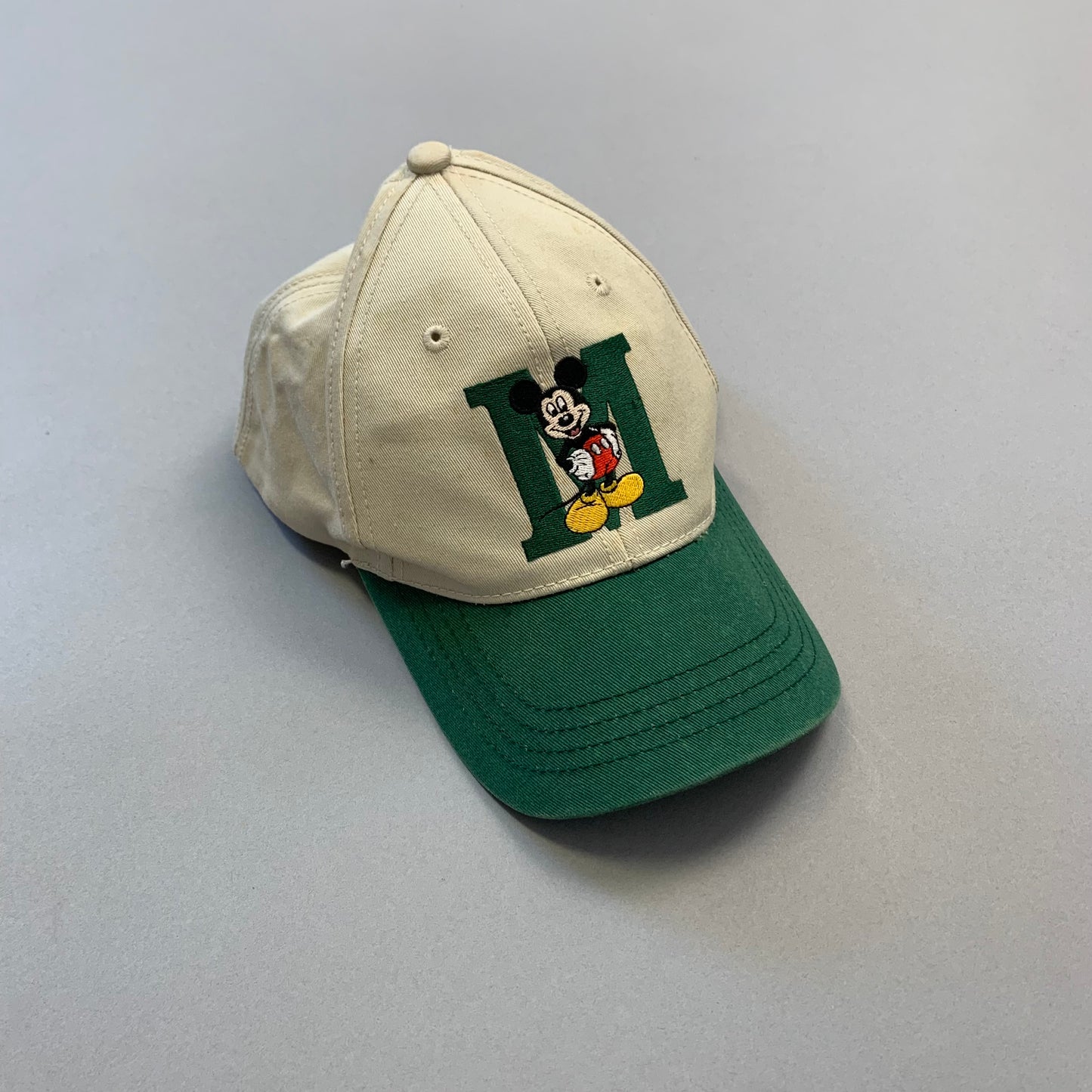 Beige cap with green brim, featuring Mickey Mouse logo.