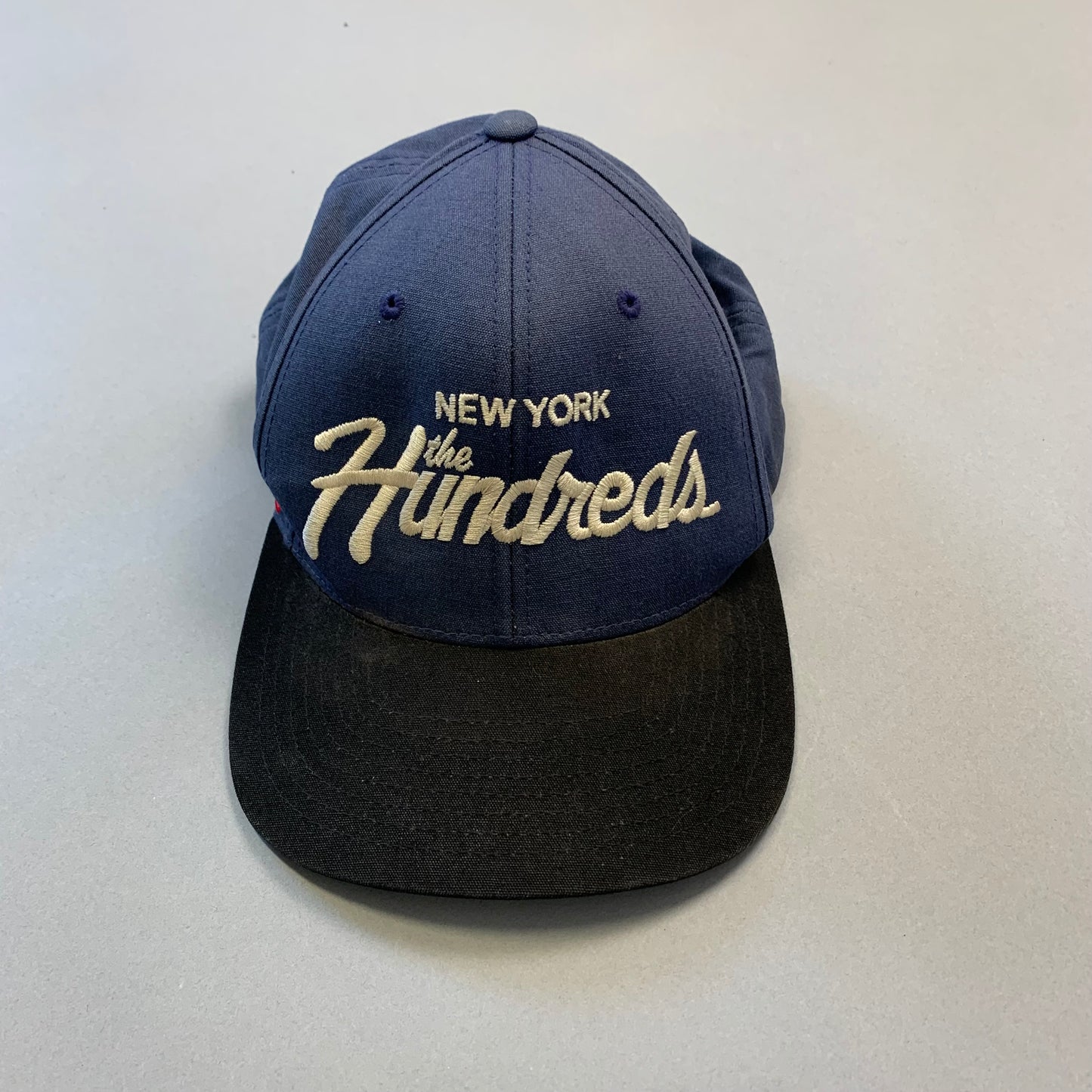 Blue nullNew York the Hundredsnull cap with black brim on grey background.